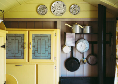 Barrow shepherd's hut kitchen area with woodburning stove, pots and pans, and kitchen unit painted in a retro yellow colour