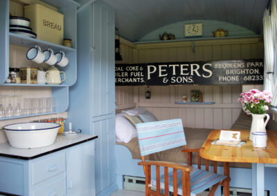 Enjoy shepherds hut glamping in Beacon hut, which is decorated in pale blues with double bed, single bunk above it, table with director's chair, kitchen cupboards for storage and enamel kitchen crockery on show