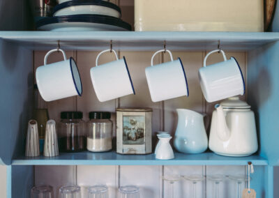 Enamel kitchenware, salt and pepper pots and teapot with plates, bread bin and glassware on the shelving in Beacon shepherd's hut