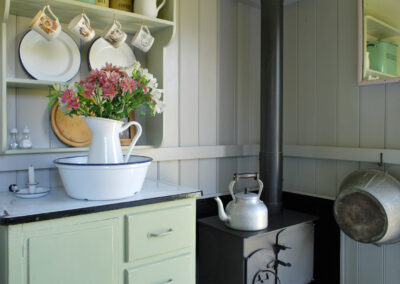 Detail from Butser kitchen area with large kettle on the woodburning stove, large cooking pan hanging on the wall and painted dresser
