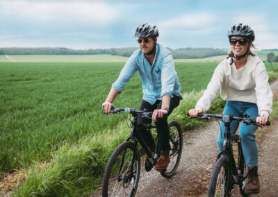 Couple cycling wearing sunglasses and cycling helmets with view of the South Downs behind them on a sunny day