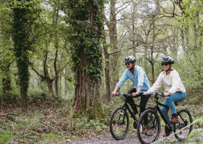 Young couple wearing cycle helmets and cycling through ancient woodland in the South Downs