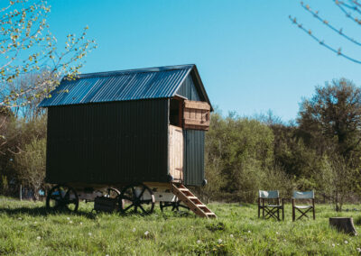 Exterior of Little Sheepwash shepherd's hut in Hampshire with wooden steps, stable door open and outdoor seating on a sunny spring day with clear blue sky