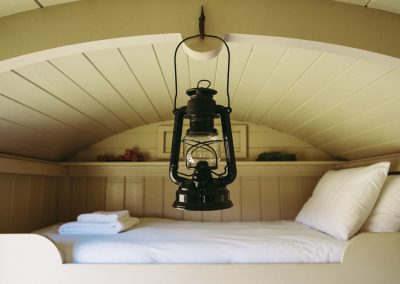 Black and unlit hurricane lamp hanging from the ceiling of one of our Shepherd's Huts with bunk bed. FInd out more about our guest information on this page