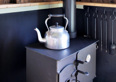Large stainless steel kettle on top of the woodburning stove in Little Sheepwash with companion fire set hanging beside it