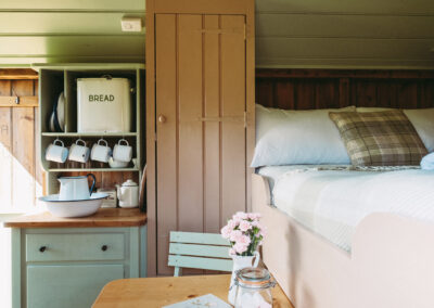 Living area in Little Sheepwash shepherd's hut with wardrobe, slide-out table and chair, double bed and washstand, cupboard and enamel kitchenware