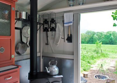 Kitchen area in Old Winchester with woodburning stove and kitchen equipment hanging on the wall, stable door open to the paddock and grassy meadow beyond