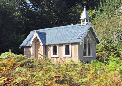 Exterior of St Brides with ferns growing in front and woodland behind on a sunny day
