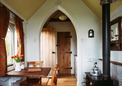 Interior of St Brides tiny glamping house, in the style of a chapel with wooden furniture, an arched ceiling and woodburning stove