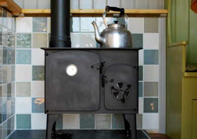 The Wriggly Inn woodburning stove with large kettle on top and tiled surrounding wall