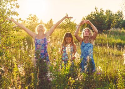 Three young girls playing on the meadow on a sunny summer evening