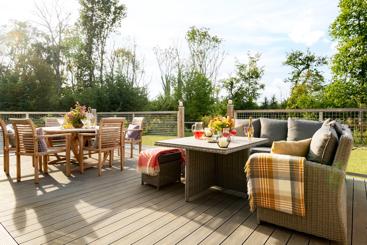 A beautiful summer evening on the deck of Portuguese Laurel, Grenville at Wallops Wood with cosy throws and cushions over the rattan furniture, and the outdoor dining table laid for an al fresco meal